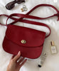 Red handbag with a hand holding it, surrounded by small items on a light background
